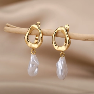 Close-up of golden irregular metal earrings with baroque pearls hanging on wood branches