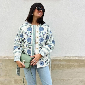 Detailed close-up of a white quilted cotton jacket with blue floral embroidery and buttons