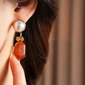Close-up of golden pearl earrings with orange resin drop on female model