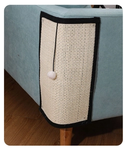 Detail of natural sisal cat scratcher mat protecting sofa corner with white plush ball