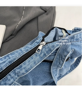 Detailed close-up of the smooth black zipper and silver hardware on a blue denim tote bag