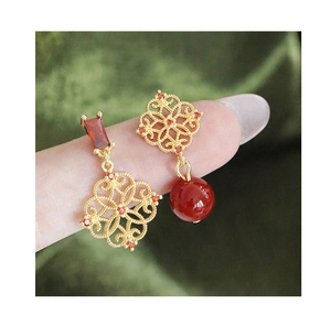 Macro detail of vintage hollow flower earrings with red zircon and gold plated finish