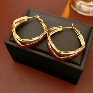 Detailed close-up of double-layered twisted gold and dark red enamel hoop earrings