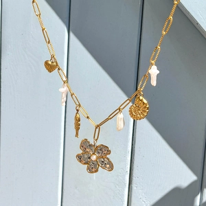 Collier doré style océan avec perles, pendentifs cœur, poisson et coquillage sur bois bleu