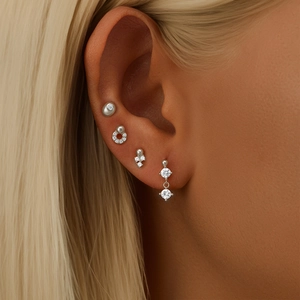 Close-up of four minimalist silver heart earrings with zircon and pearls on ear