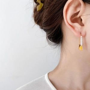 Elegant gold safety pin earrings with five white pearls on a minimalist model profile
