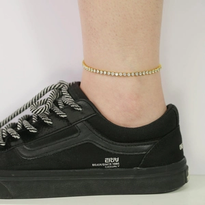 Close-up of a gold tennis anklet with round white zircons worn on the ankle