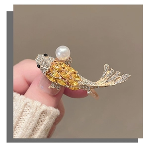 Detail of golden koi fish brooch with yellow gemstones and a white pearl accent