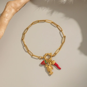 Detail of 18K gold plated bracelet featuring strawberry, lobster, and red horn charms