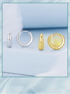 Minimalist gold and silver polished hoop earrings on soft blue background with feathers