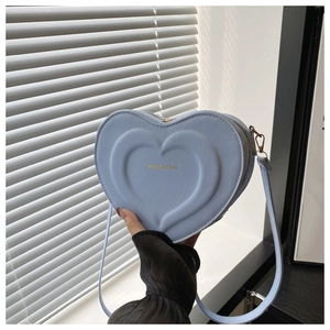 Close-up of heart-shaped crossbody bag in light blue faux leather with gold fashion text