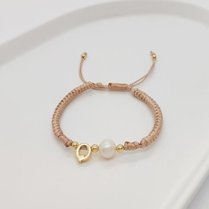 Detailed shot of handmade woven bracelet with white pearl and gold letter Q charm