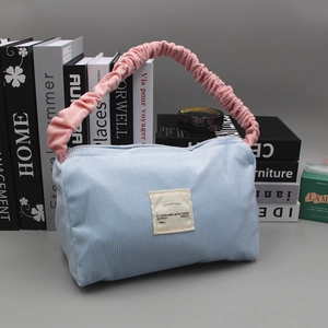 Detail of light blue corduroy handbag with pink ruffled handle and beige woven label