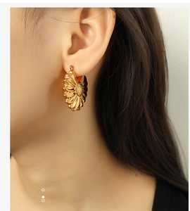 Detailed view of large gold hollow flower petal earrings worn by a female model