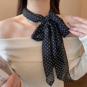 Close-up of a black polka dot silk scarf tied in a bow on a model's neck for an elegant look