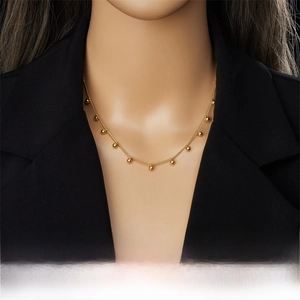 Close-up of a delicate gold chain necklace with beads worn on a black blazer