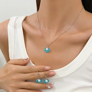 Detail of teal shell necklace and pearl earrings on model with silver chain