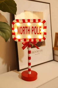 Close-up of wooden North Pole Christmas sign with LED lights and a red bow decoration