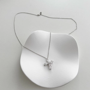 Macro shot of a silver cross pendant with faceted gemstones on a wavy textured display