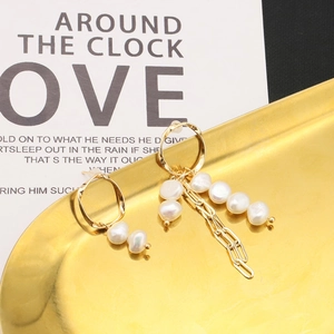 Detail of asymmetric pearl earrings with long gold chain on a golden metallic tray