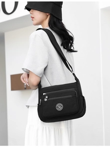 Model wearing a black nylon crossbody bag with multi-compartment design and round logo