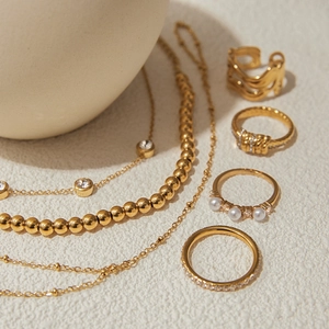 Detail of gold jewelry set featuring pearl rings and zircon bracelet on ceramic plate