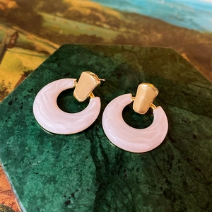Close-up of pink marble resin hoop earrings with gold accents on green base