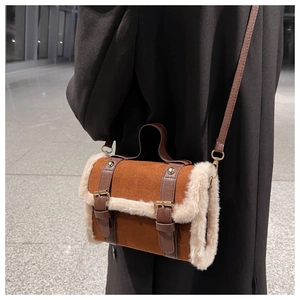Close-up of brown suede handbag featuring plush faux fur trim and leather buckle straps