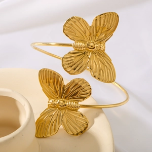 Elegant gold butterfly cuff bracelets set on a creamy textured ceramic display