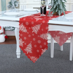 Close-up of red Christmas table runner with white trees and wavy edges on a festive table