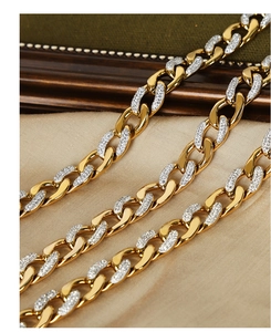 Macro view of gold-plated Cuban link necklace with inset crystals on beige satin fabric