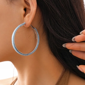 Detailed close-up of large round silver hoop earrings wrapped in light blue denim fabric