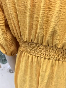 Detail of high-waist smocked elastic waist on a yellow pleated ruffle dress