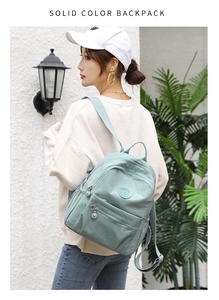 Detail view of mint green nylon backpack featuring multiple zippers and side pockets