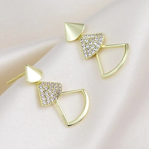 Detalle de pendientes geométricos dorados con circonitas sobre seda elegante