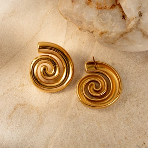 Detail of 18K gold-plated stainless steel spiral earrings on a textured stone surface