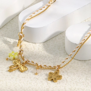 Detail of double-layer gold chain with floral charms and woven rope on white display
