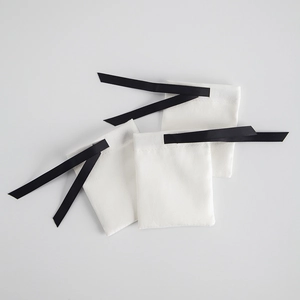 Three white microfiber jewelry pouches with black grosgrain ribbon drawstrings on gray background