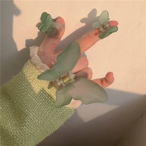 Three-piece set of matte green butterfly hair claws shown in hand under natural warm sunlight