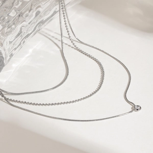 Detail of silver layered necklace featuring snake chain with round white zircon pendant