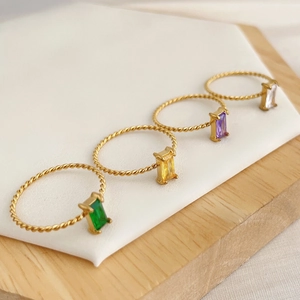 Macro detail of four gold titanium steel rings set with emerald, yellow, purple, and clear gems