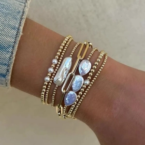 Detail shot of stacked gold bead bracelets with a baroque pearl and paperclip link chain