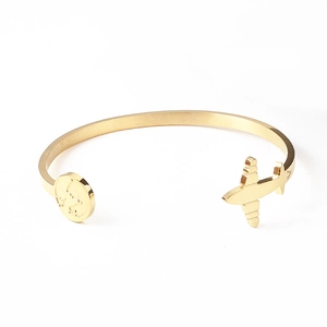 Detailed macro of gold C-shape steel bangle featuring airplane and world map engraving