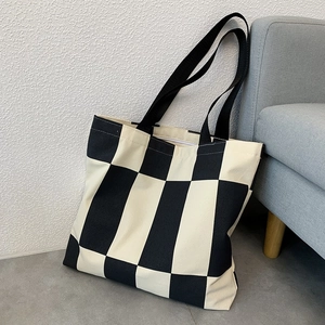 Detail of checkered canvas tote bag with black straps in a minimalist home setting