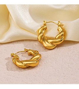 Gros plan de boucles d'oreilles créoles torsadées dorées sur satin champagne