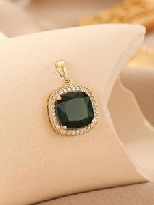 Close-up of golden four-prong pendant with deep green gem and pavé cubic zirconia