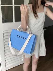 Blue woven straw tote bag with Paris embroidery held by a model in a resort style setting