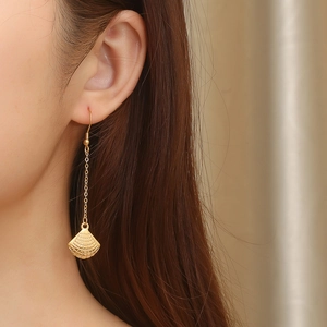 Detail of a long gold drop earring featuring a mesh textured scallop fan pendant on a model