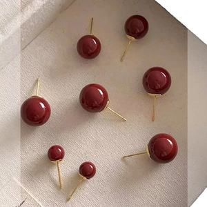 Vintage dark red ball stud earrings with gold pins in various sizes on beige linen fabric