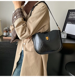 Side view of black saddle bag in glossy textured leather with gold metallic buckle